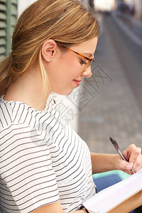 年轻女子在书中用钢笔写字的侧面肖像图片