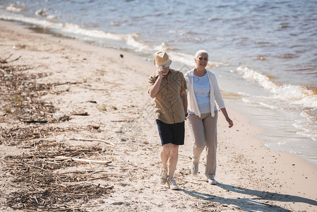 幸福的老年夫妇手牵走在河边的沙滩上图片