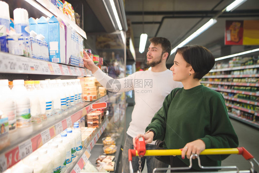 一个积极的年轻夫妇从超市货架上捡起牛奶并微笑在超市进行家庭购物图片