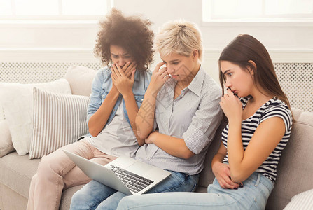 三名哭泣的妇女使用笔记本电脑观看悲哀电影或阅读震惊新闻浏览和搜索家图片