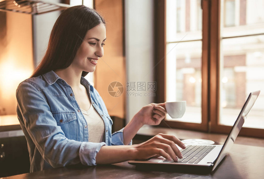 美丽的女孩在用笔记本电脑喝咖啡和微笑时图片