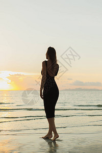 日落时赤脚站在海沙滩上的迷人女图片