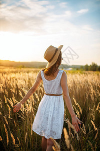 日落时在小麦田中行走的白色妇女服装和草帽图片