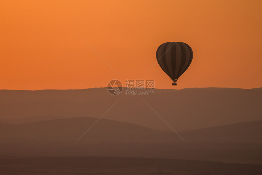 一个热气球飞过树木繁茂的山丘图片