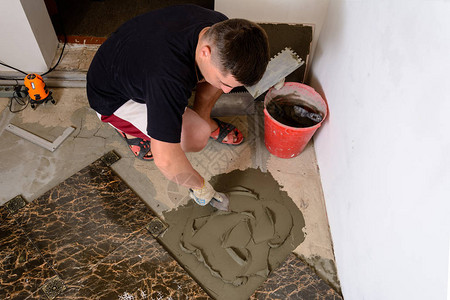 师傅在水泥表面用胶水溶液铺盖大理石砖时推着一个有胶图片