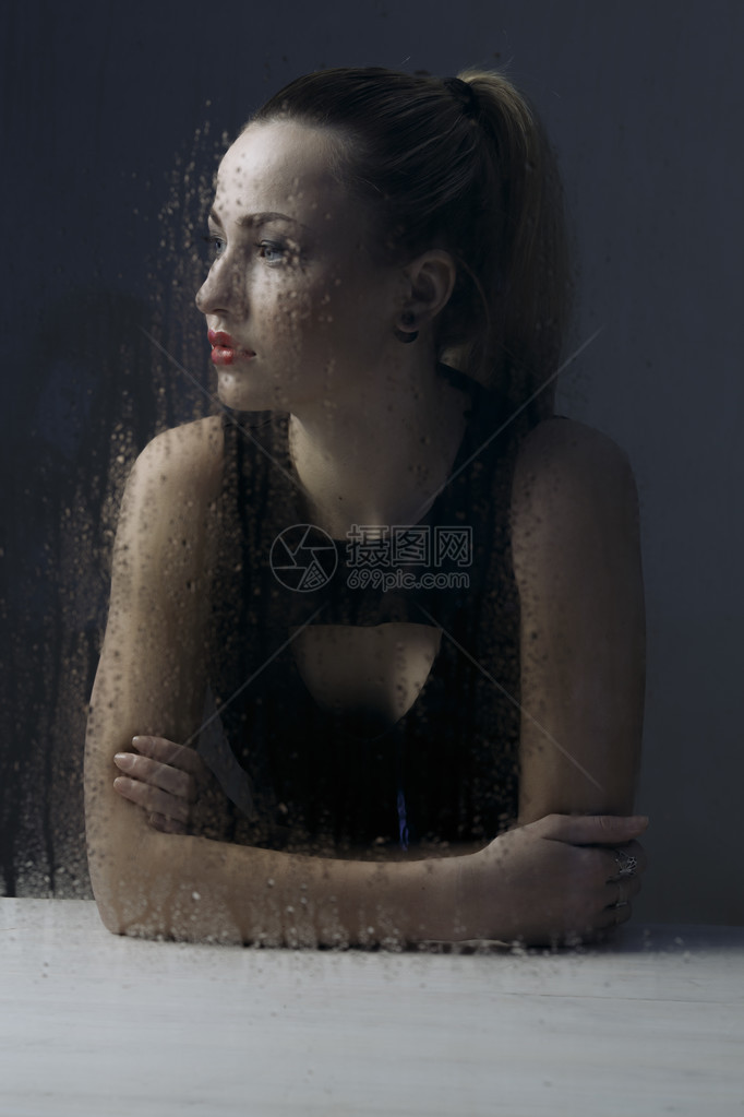 坐在窗后满是雨滴的窗户后面的单身妇女感到沮丧图片