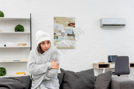 身着温暖衣服坐在家中沙发上有空气状况挂在背景上的年轻女图片