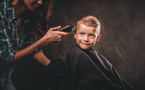 有修剪器的儿童理发师正在深色背景下切割小男孩心满意足的可爱学龄前图片