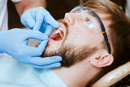检查并选择牙医椅上牙齿的颜色牙医使英俊的年轻高清图片