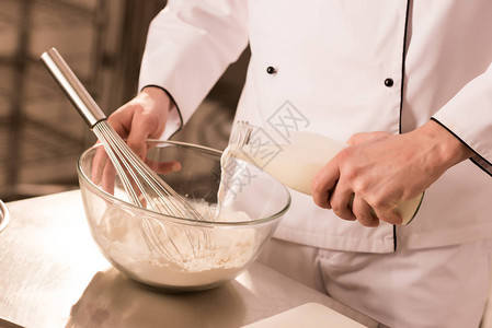 在餐饮厨房中将牛奶加到面粉中的图片