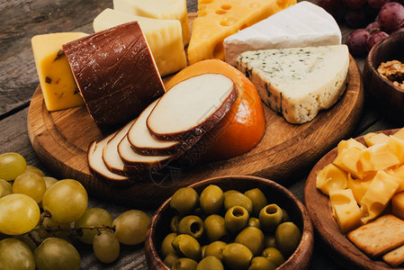 近距离观察木制切菜板上的各种奶酪附近的橄榄和葡萄图片