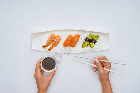 在吃白边孤立的寿司时拿着筷子和加酱油图片