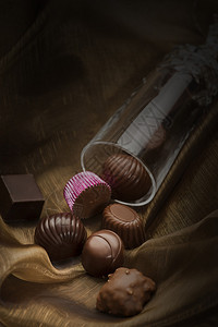 玻璃管中手工制作的不同形状和口味的豪华巧克力溢出到柔软的织物上图片