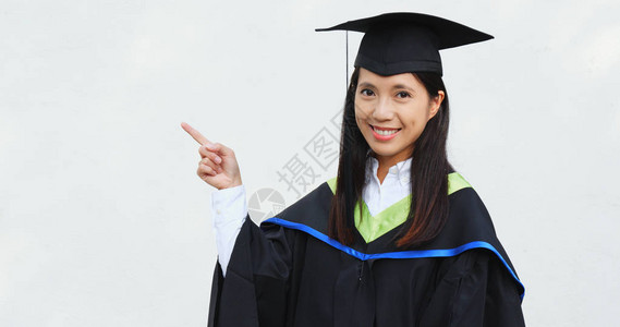 毕业礼服和手指点放在一边的女学生图片