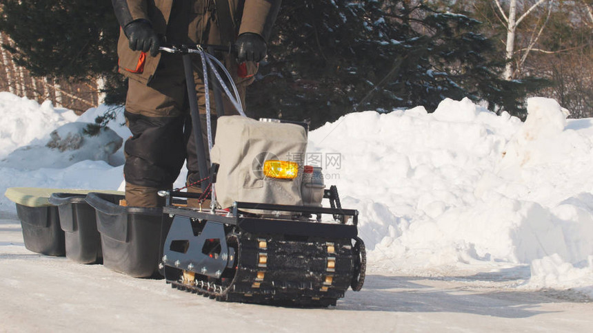 在冬季道路上骑着带拖车和乘客的履带式迷你雪地摩托的男图片