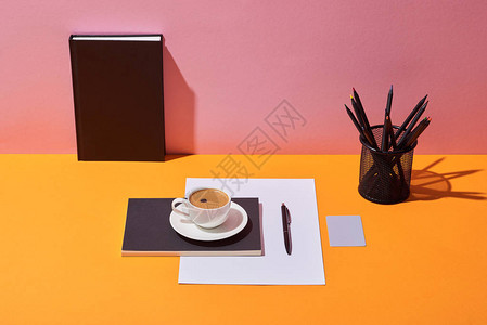 黄桌和粉红背景的咖啡杯碟子笔纸页铅笔持图片
