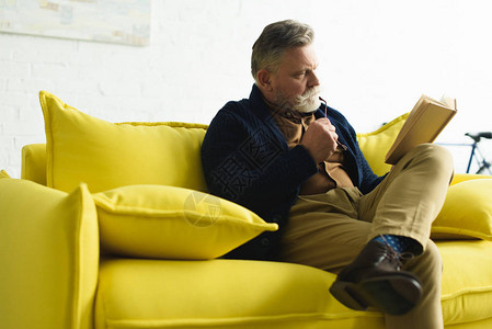 大胡子老人坐在黄色沙发上看书图片