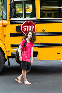 年轻女孩站在校车旁的垂直照片图片