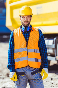 身穿反射背心和硬帽的工人站在大黄卡车前的建筑工地图片