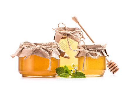 玻璃罐木制蜂蜜花瓶和含薄荷叶的甘菊果酱中新鲜甜蜜蜂的近视图片