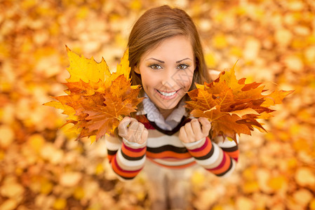 可爱的年轻女子在阳光明媚的森林中享受秋天的色彩她拿着金黄色的叶图片