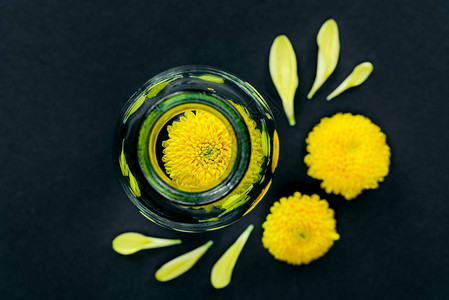 黑面上散落的玻璃瓶和花瓣中黄色花朵构成图片