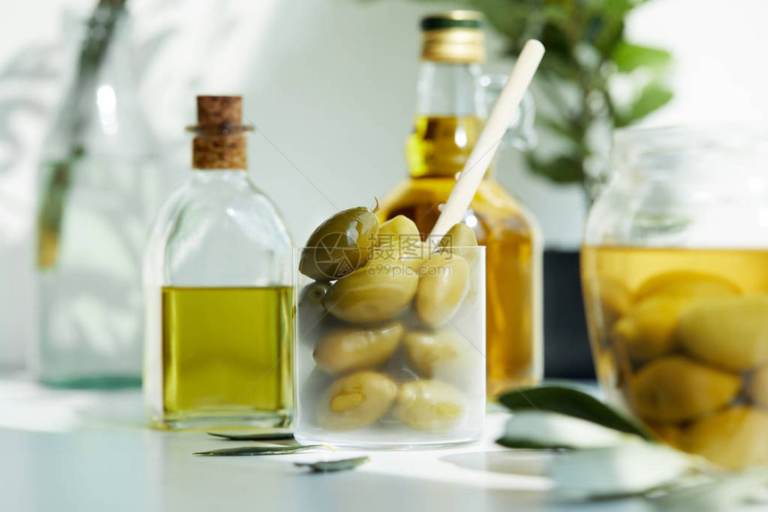 用玻璃勺绿橄榄罐子各种香味橄榄油瓶和白桌上图片