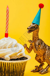 有选择的焦点玩具恐龙在派对帽上在蛋糕旁边图片