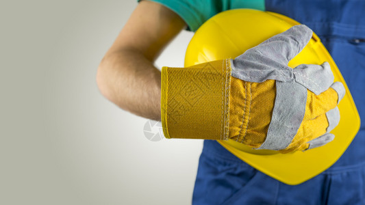 戴防护手套的工人拿着黄色安全帽或安全头盔图片