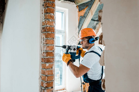 制服手套和黄色手套工人在砖墙上用锤子钻打的钢图片