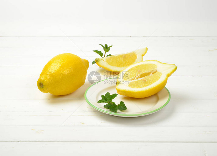 白盘和木质背景上的整个柠檬和切片柠檬图片