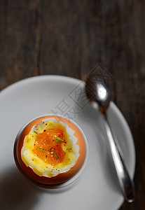 木制背景蛋杯中的软煮鸡蛋图片