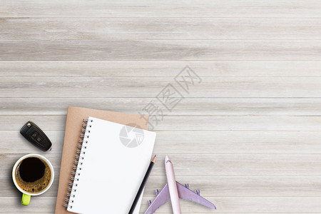 笔记本铅笔与咖啡车钥匙和飞机在白色木桌背景顶视图与设图片