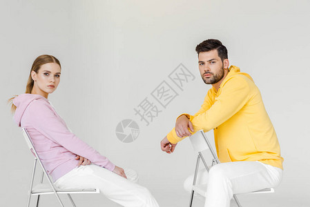 身穿粉色和黄色连帽衫的年轻男女模特坐在椅子上图片