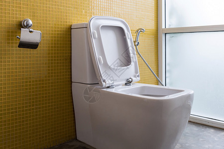 现代厕所内室的白色抽水马桶和黄色墙图片