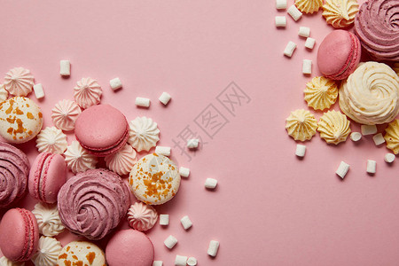 粉碎美味的甜蛋白甜饼杏仁饼和粉红色背景上的小棉花糖片图片