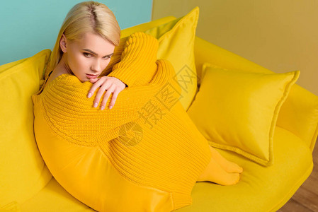 身穿黄色毛衣和坐在黄色沙发上的紧身裤的年轻柔图片