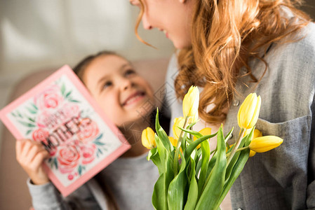 持有黄色郁金香和快乐母亲日贺卡的母亲和女儿的选择焦点图片