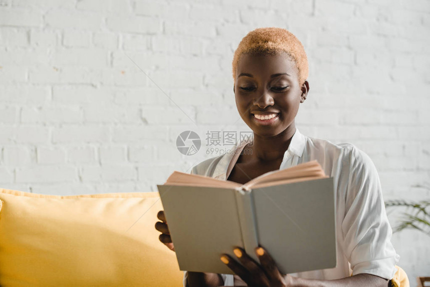 在黄色沙发上剪短头发阅读书的非洲女喜图片