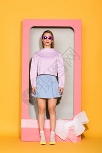 在太阳镜中的年轻时尚女模特站在装饰盒旁边弓图片