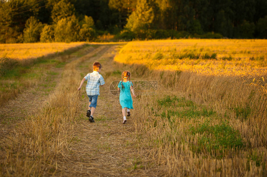 一个男孩和一个穿着蓝色连衣裙的女孩在温暖而阳光明媚的夏日傍晚在麦田里奔跑日落时黑麦田图片