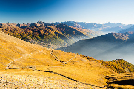 在秋天日落时穿过高山坡和多彩草地的泥沙山路背景图片