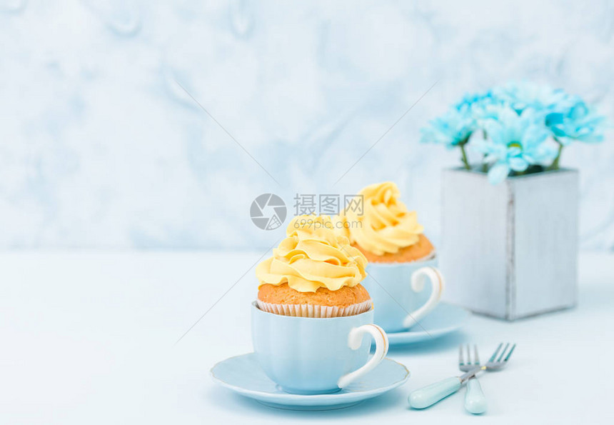 带有黄色奶油装饰和蓝色菊花束的纸杯蛋糕图片