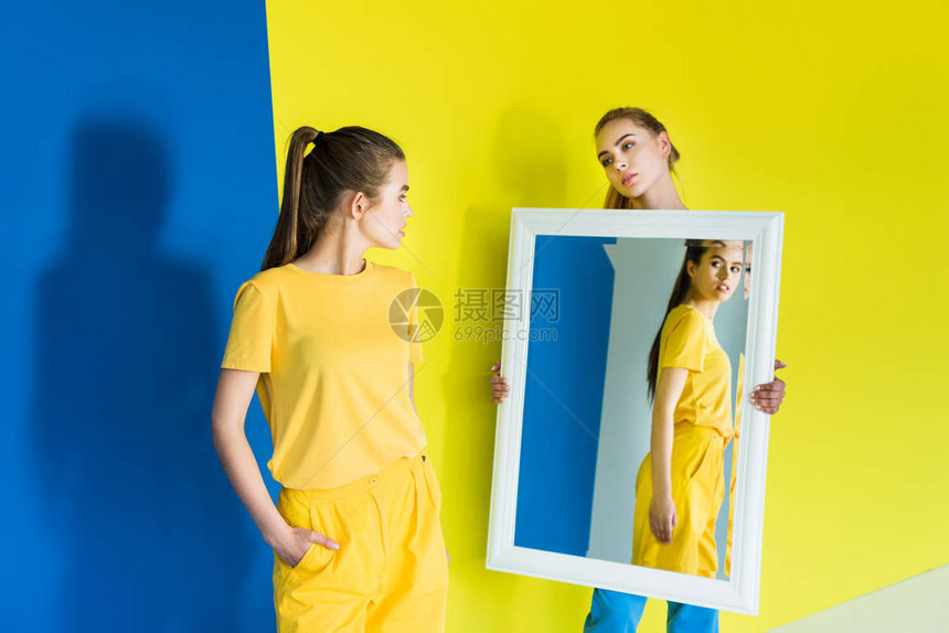 有吸引力的年轻女孩为蓝黄背景的朋友拿着镜图片