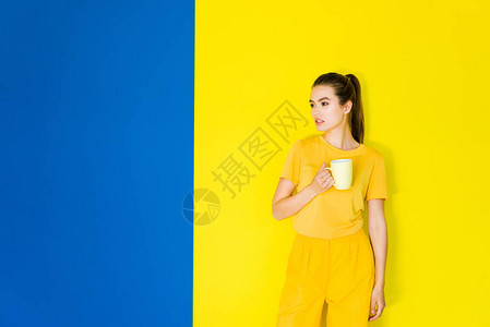 女模特在蓝色和黄色背景上手拿着杯图片