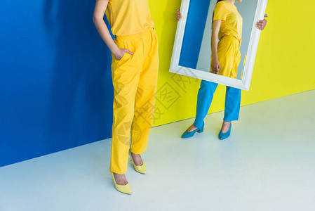 以蓝和黄色背景在镜子前试穿衣服的妇女被割图片