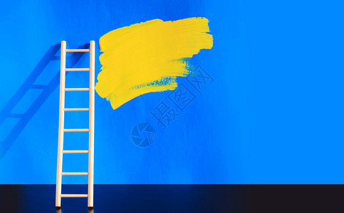 绘画概念蓝墙附近的木制梯子和黄色的油漆图片