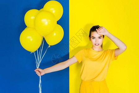 高贵的黑褐色女人拿着一堆黄色气球在蓝色背景图片