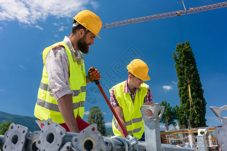 两名高效的蓝领员工在建造金属脚手架前准备物资图片