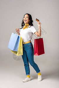 持有彩色购物袋和在灰色上显示信用卡的亚洲妇女服图片